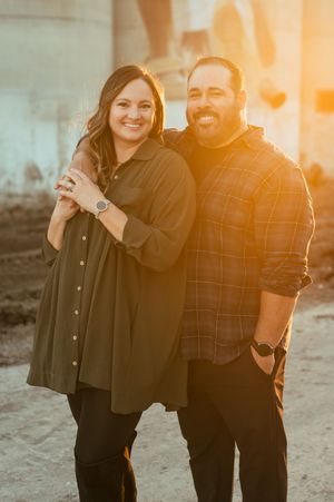 A couple poses together outdoors at sunset, with warm golden lighting creating a romantic atmosphere.