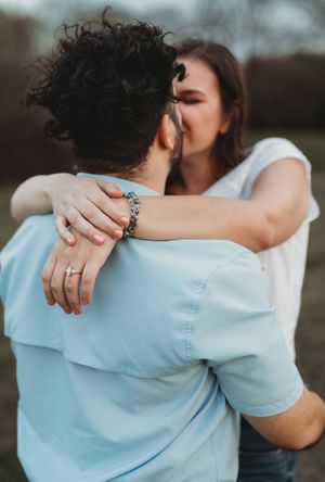 A romantic couple embraces intimately outdoors, with a bracelet visible on one arm and focus on their hands and embrace.