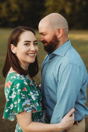 A couple shares an intimate moment outdoors, with the woman wearing a green floral dress and the man in a blue button-down shirt.