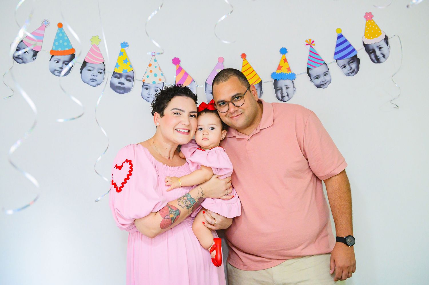 A family poses together against a white wall decorated with colorful party hat garland for a celebration.