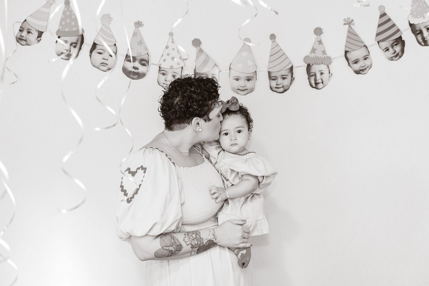 A black and white photo shows a parent and baby at a party with decorative banners hanging above them.