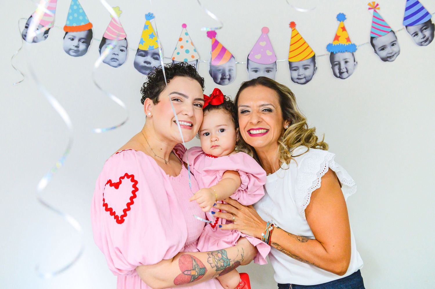 Happy family celebration scene with pink and white outfits under decorative party hat banner garland.