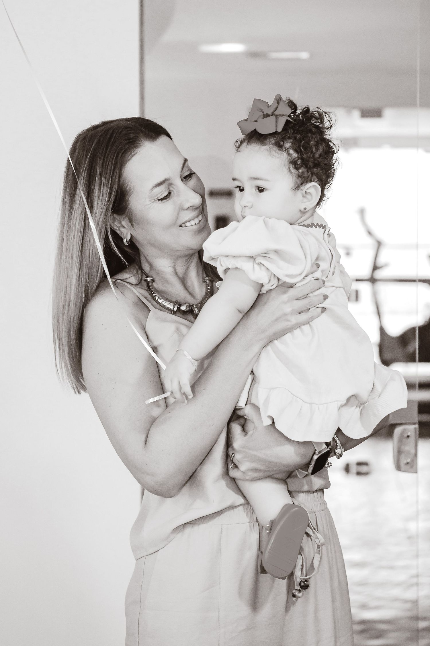 A tender black and white portrait showing a loving embrace between a parent and baby in light, airy surroundings.
