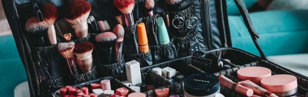 A collection of cosmetics and makeup products displayed in an open case against a teal background.