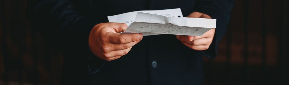 Hands holding white paper or document against dark background.