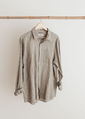 A beige linen button-down shirt hangs on a wooden hanger against a white wall.