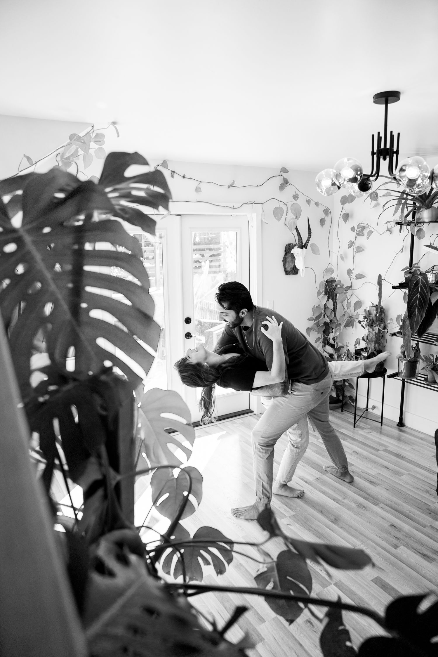 A black and white photo of dancing in an interior space with monstera plants visible in the foreground.