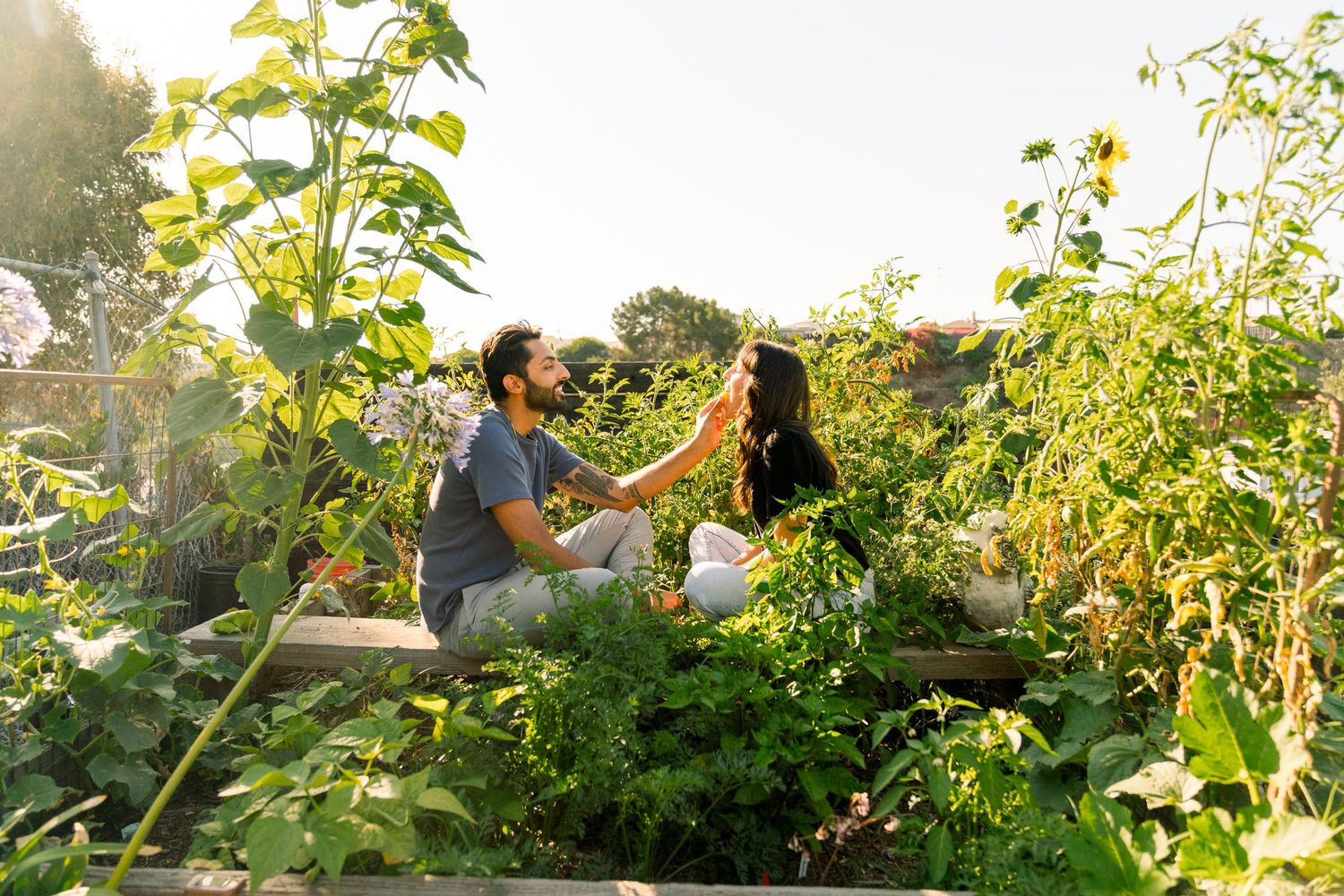 Two people share a romantic moment in a lush garden surrounded by sunflowers and greenery during golden hour.
