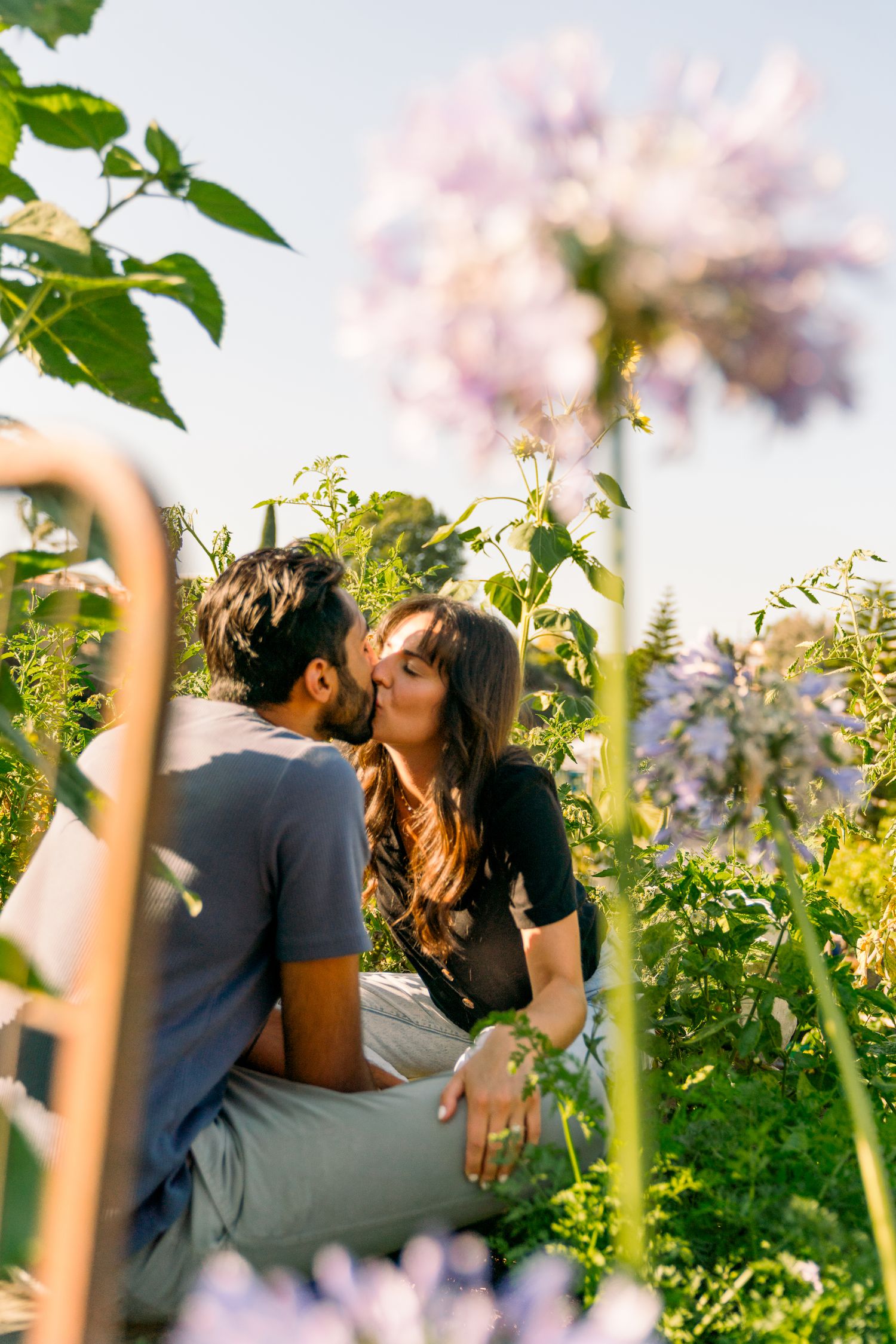 A romantic moment captured in a garden surrounded by blooming flowers and greenery.
