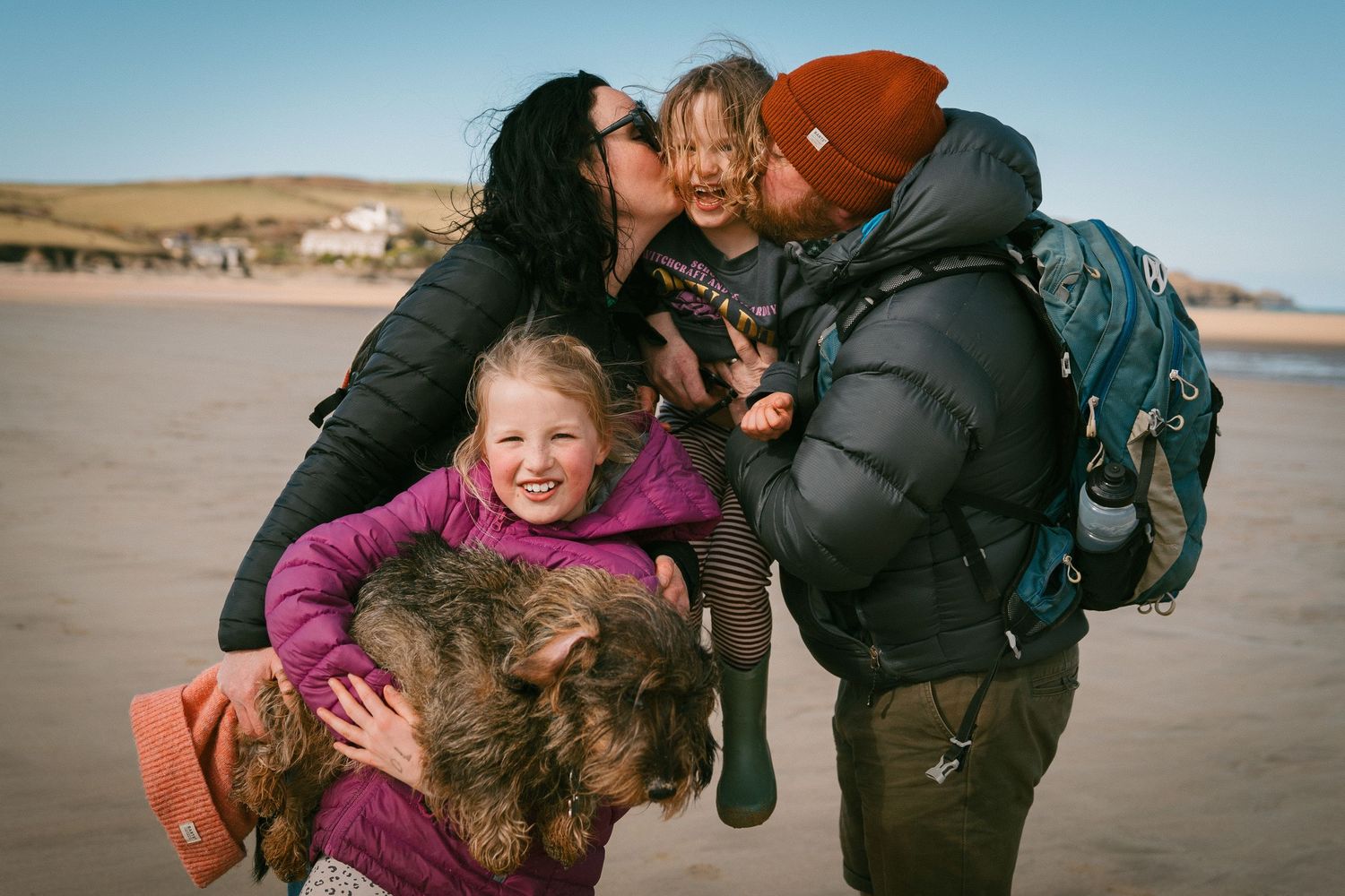 People enjoying a playful moment on the beach with their happy brown dog on a sunny winter day.