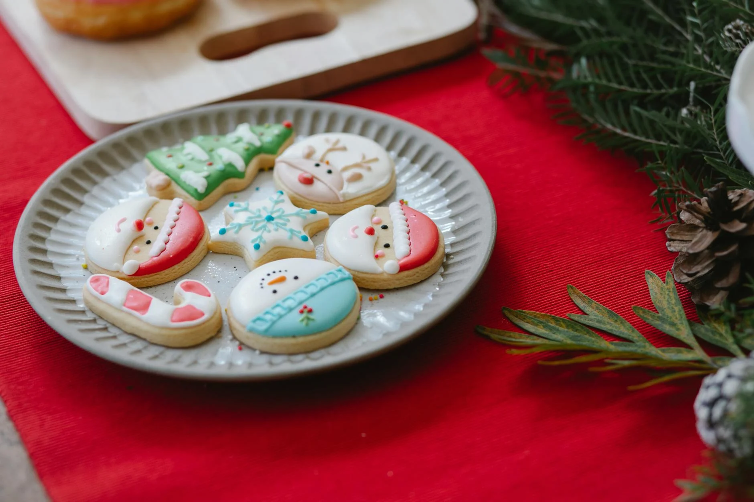 Decorated Christmas sugar cookies with blue and white icing arranged on a gray plate with a red tablecloth.