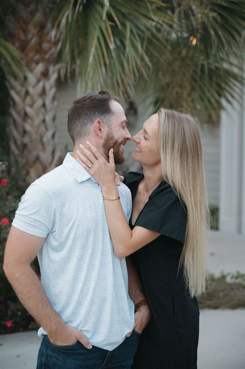A romantic couple shares an intimate moment outdoors with palm trees in the background.