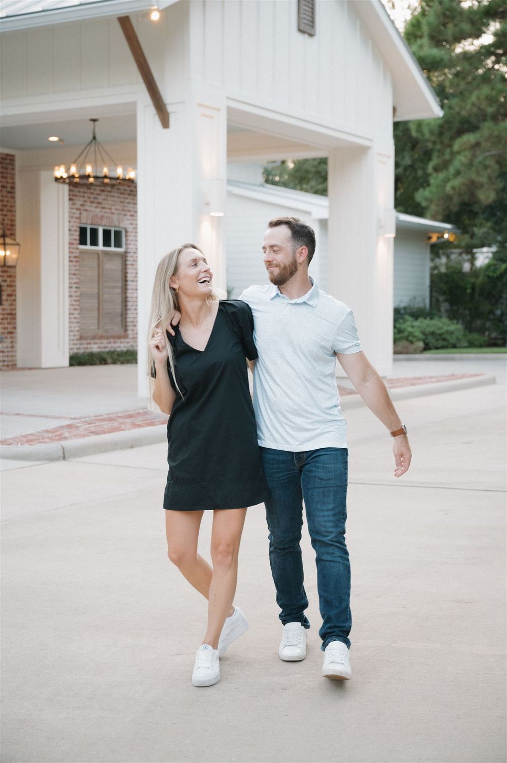 A couple walking outside a modern church entrance with white columns and brick walls laughing together.