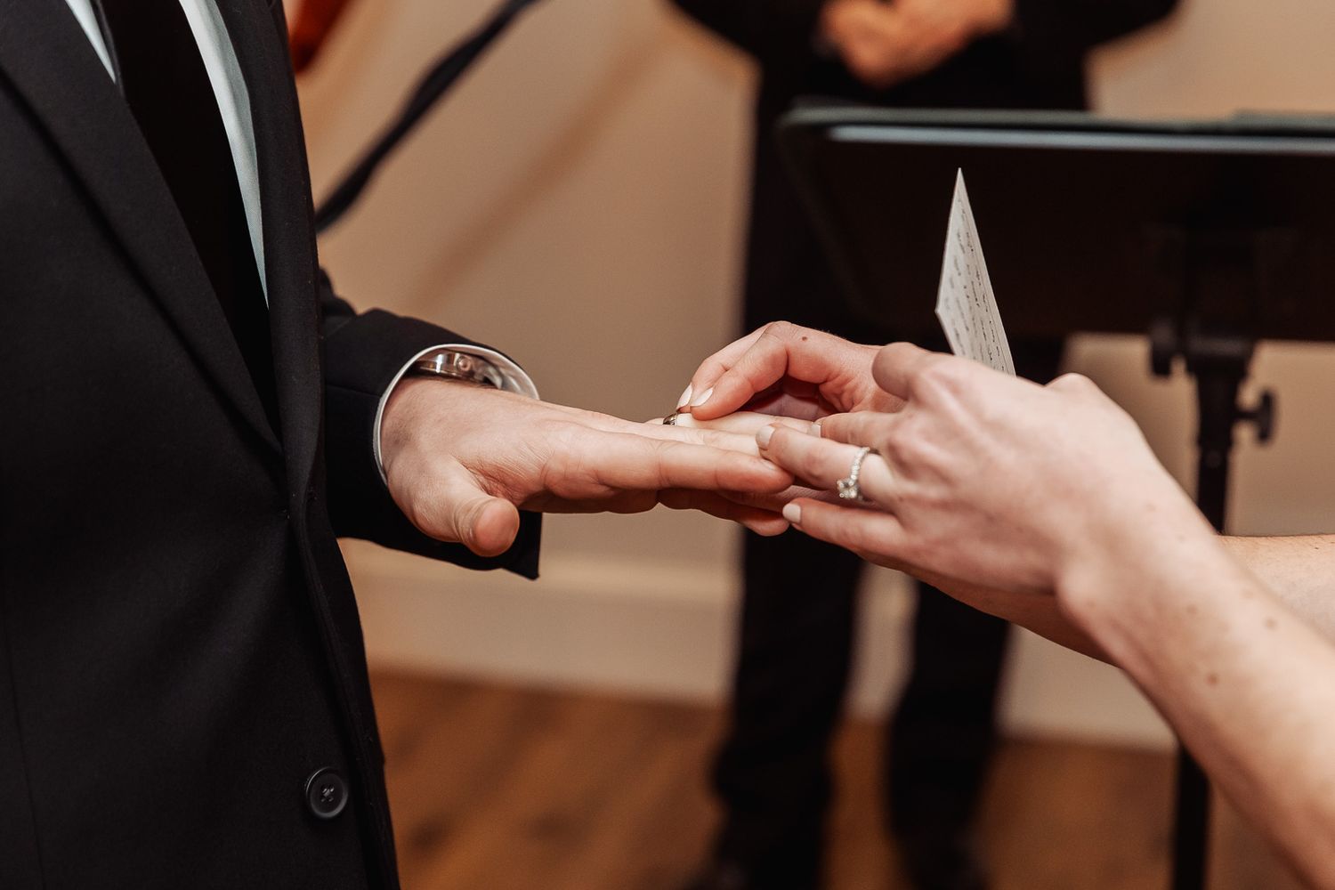 Exchanging wedding rings during a ceremony with focus on hands placing ring on finger.