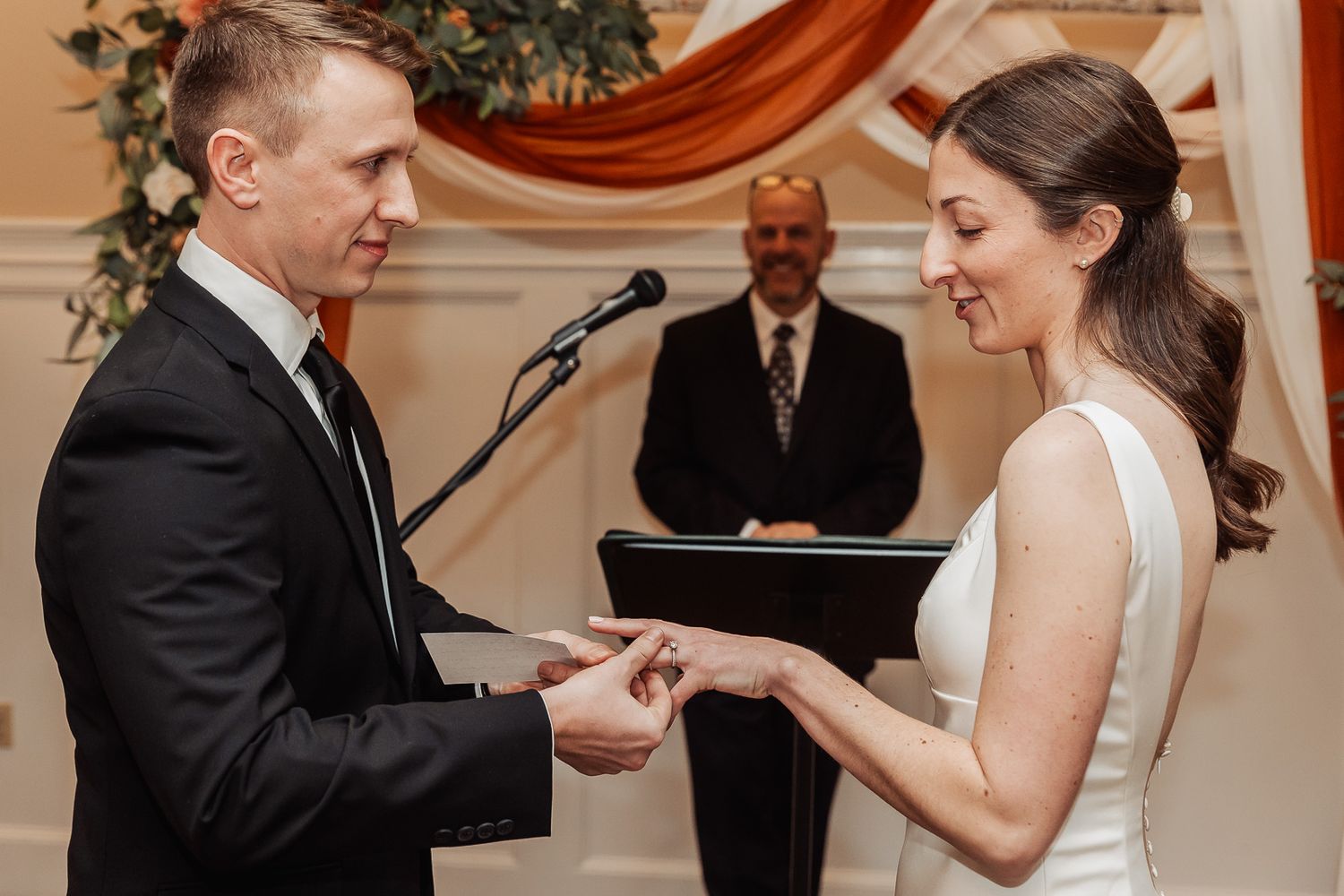 A wedding ceremony shows a couple exchanging rings during their vows in an elegant indoor venue.