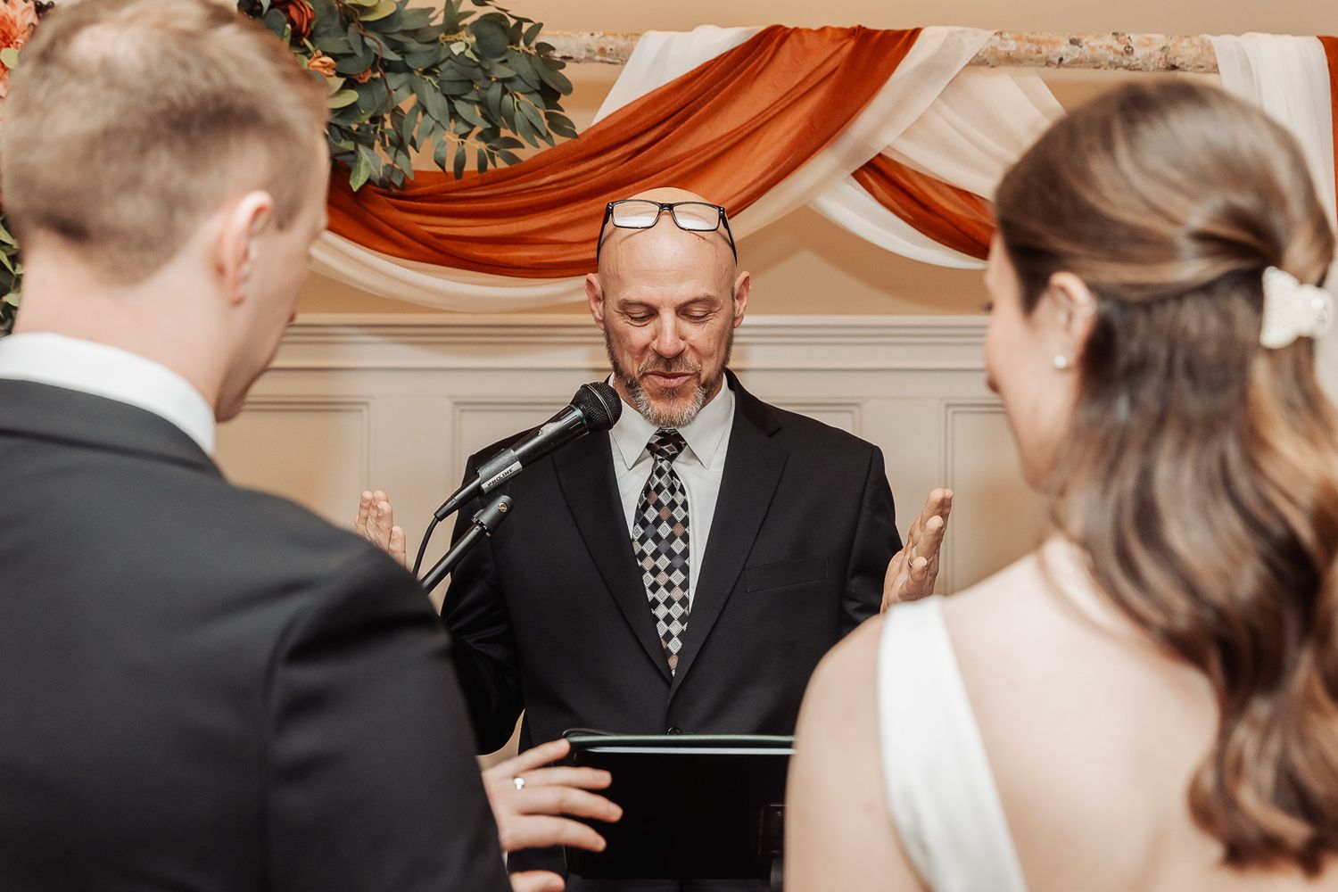 Wedding ceremony with officiant reading from book while couple listens during intimate indoor service.