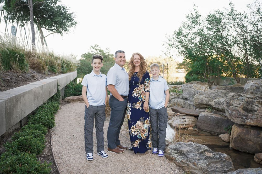A group of four people pose together on a winding path surrounded by rocks and greenery in an outdoor setting.
