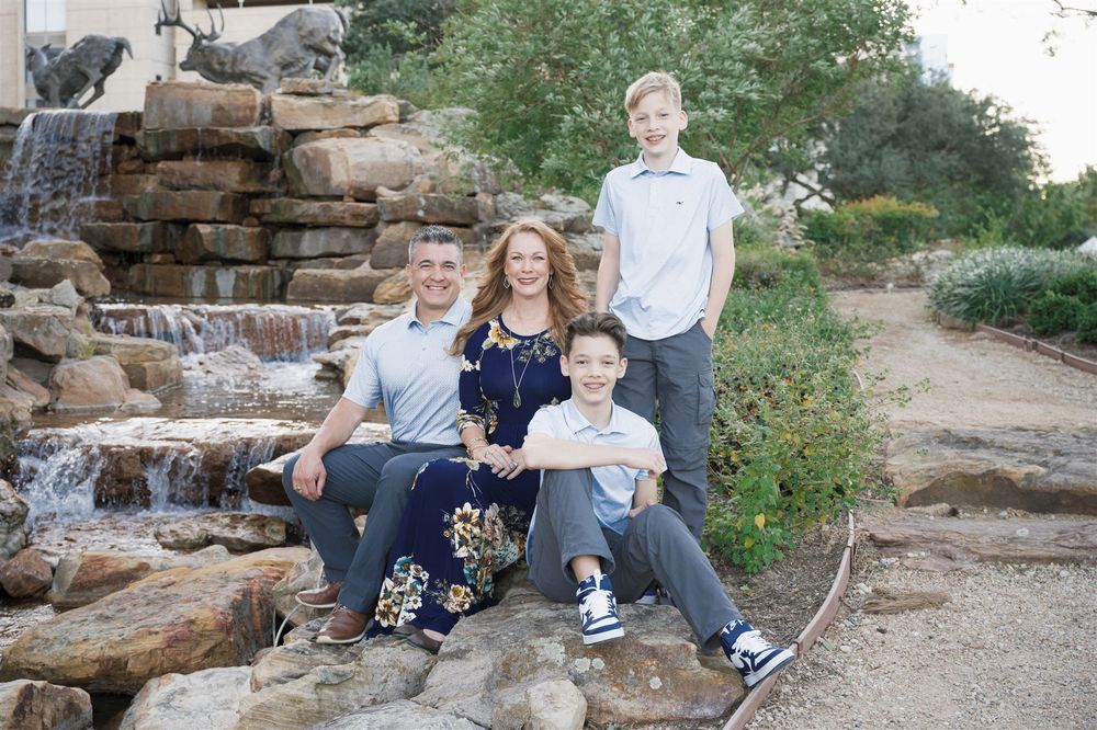 Family in casual attire sitting together on natural stone steps in an outdoor garden setting.