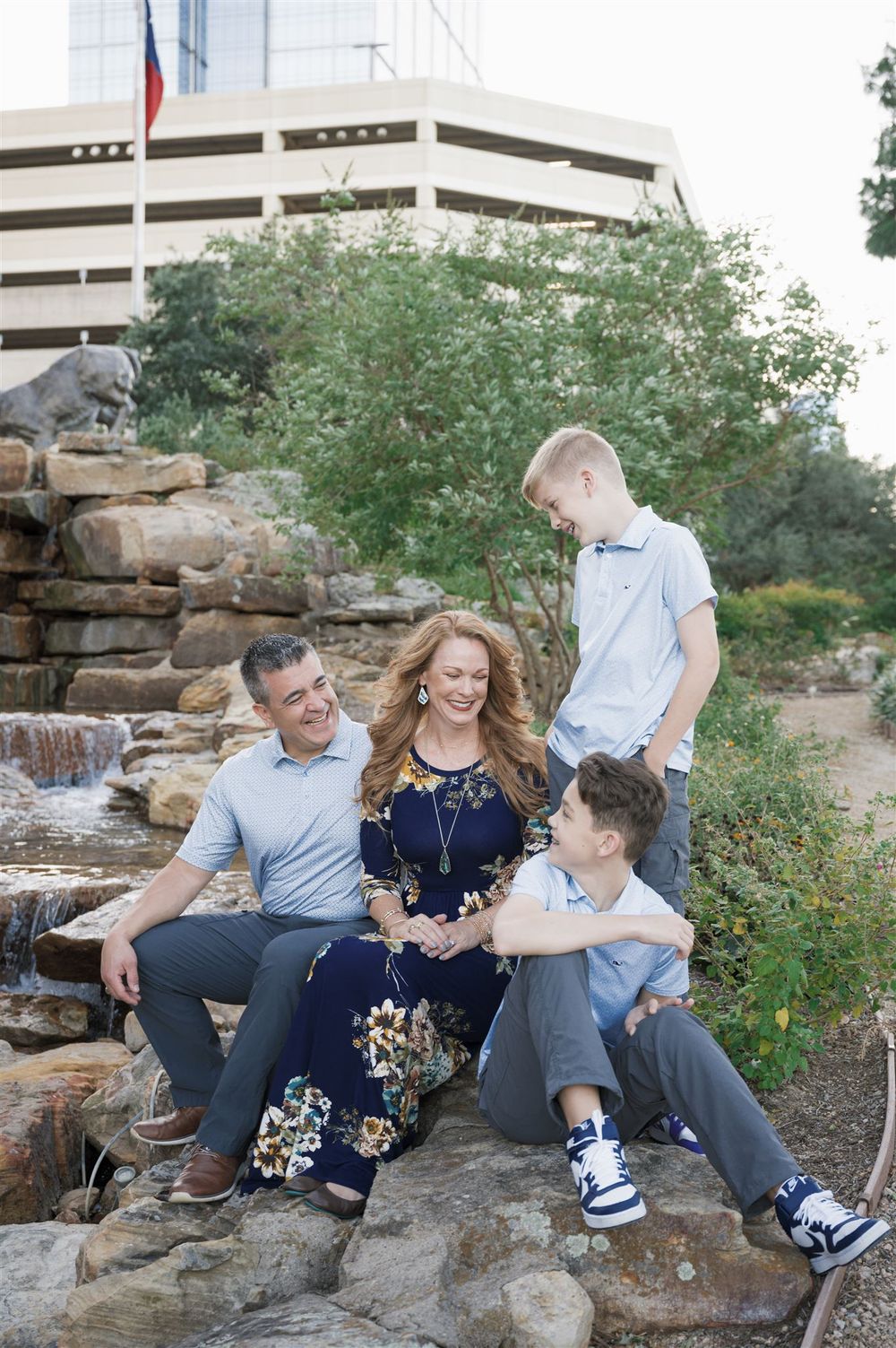 A family sits together on stone steps by a waterfall feature with an office building visible in the background.