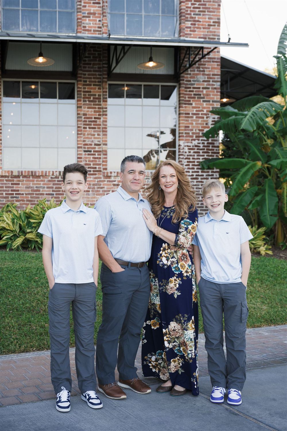 A family poses together in front of a brick building with large windows and outdoor lighting.