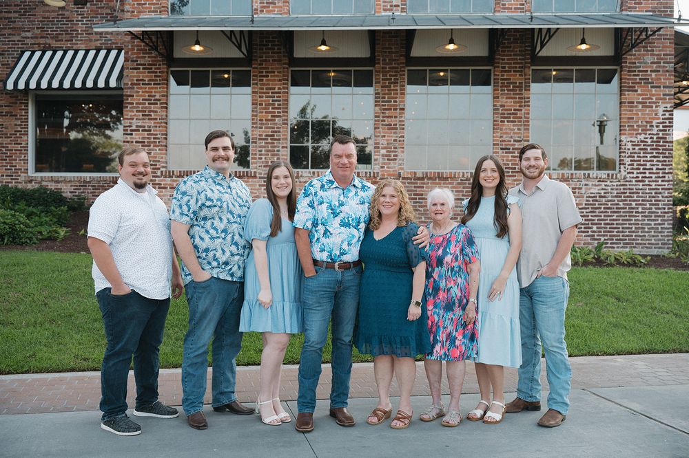 Group of people in coordinating blue and neutral outfits standing together outside a brick building with awnings.