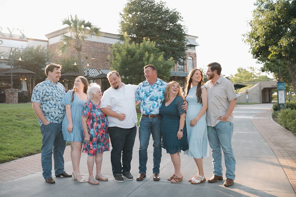 A group of friends wearing casual attire stand together outdoors on a sidewalk during golden hour.