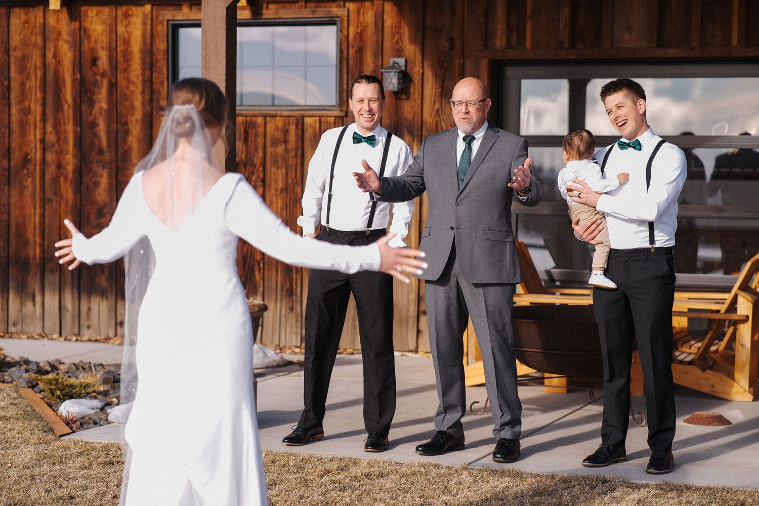 Rustic wedding scene on a wooden deck with a bride in white dress showing her gown to attendees.