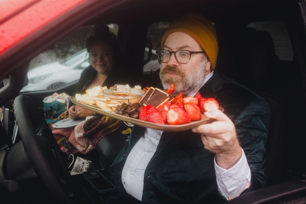 A person in formal wear eats sushi in the driver's seat of a car.