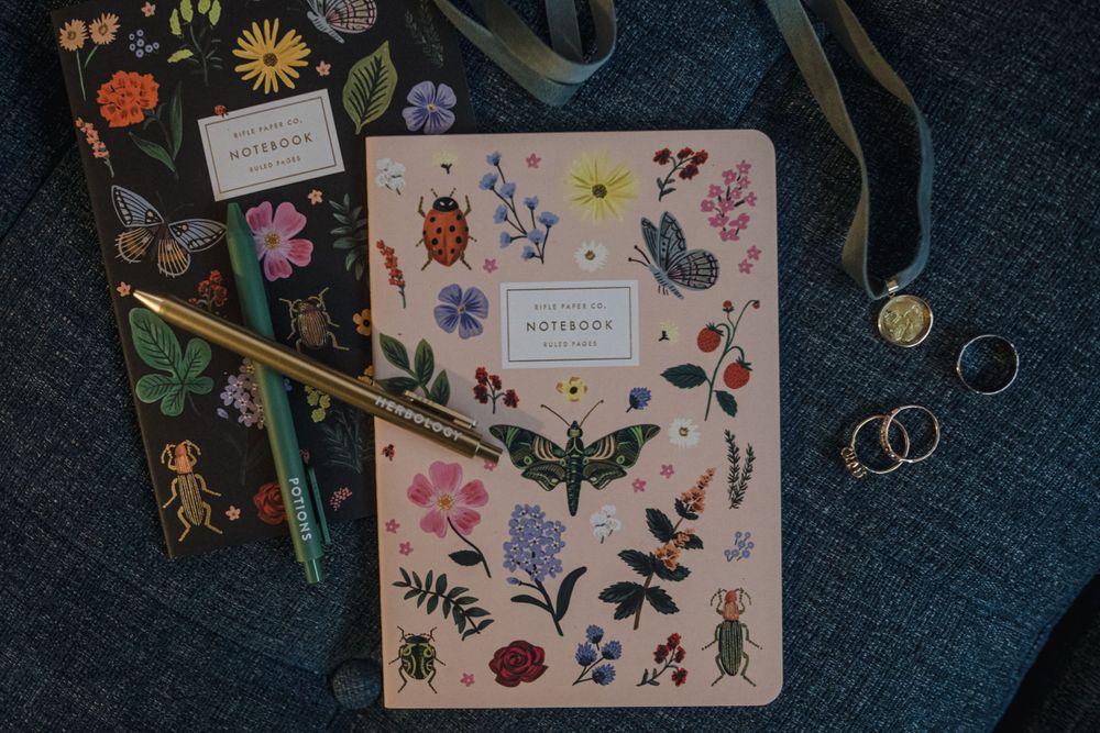 Floral and insect patterned notebooks with decorative accessories on dark fabric.