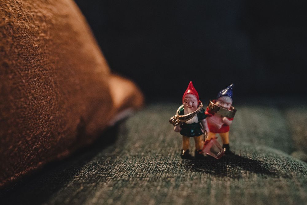 Two tiny decorative gnome figurines posed on a textured surface.