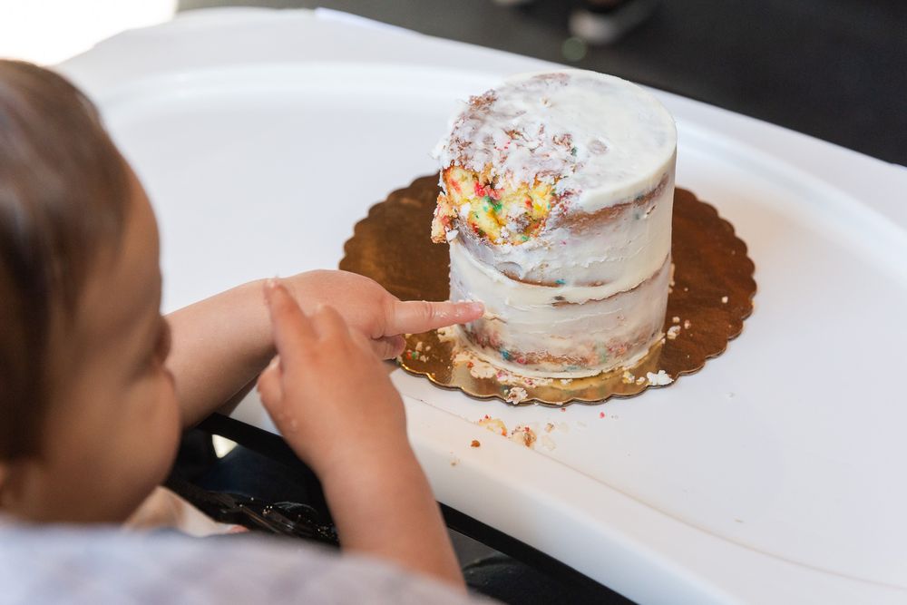 Small white cake with sprinkles on a brown plate being touched by small hands.