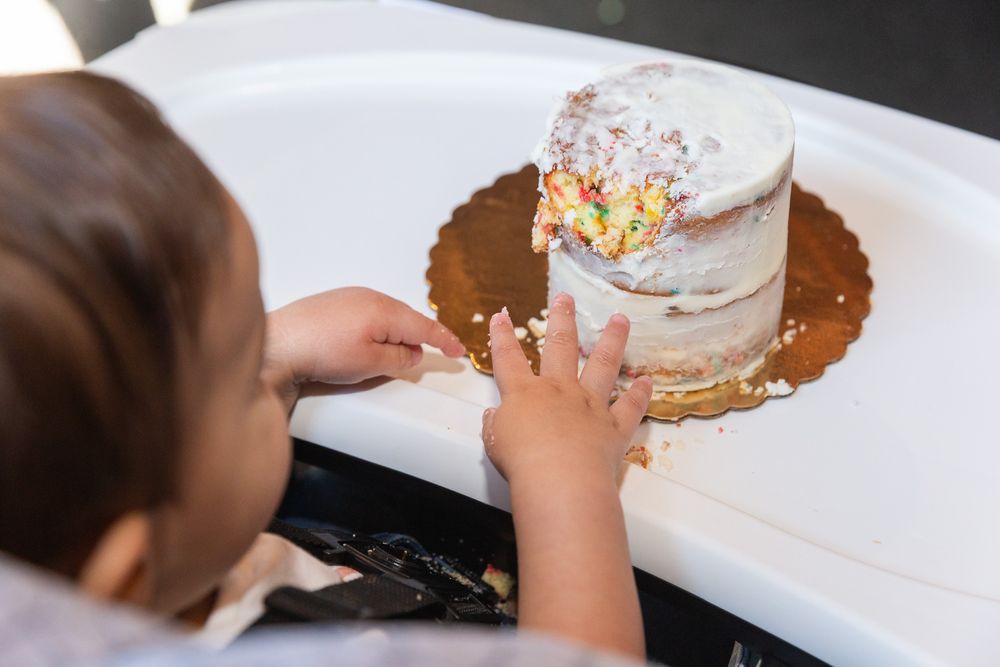 Close-up of tiny hands reaching for a decorated white cake on a highchair tray.