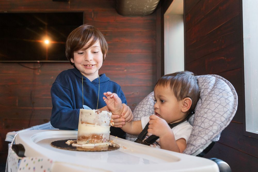 Two children sitting at a table with a small cake between them.