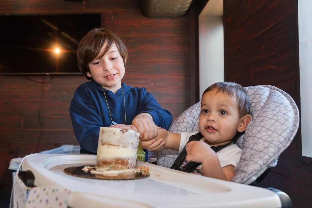 Two children sharing a moment at a table with cake in a room with exposed brick walls.