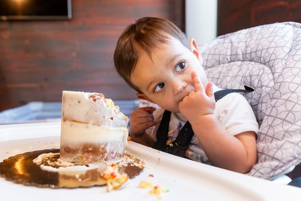 Child in gray highchair looking mischievous after eating cake.