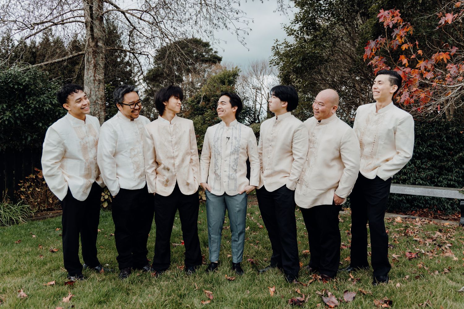 A group in matching white formal jackets poses outdoors during autumn.