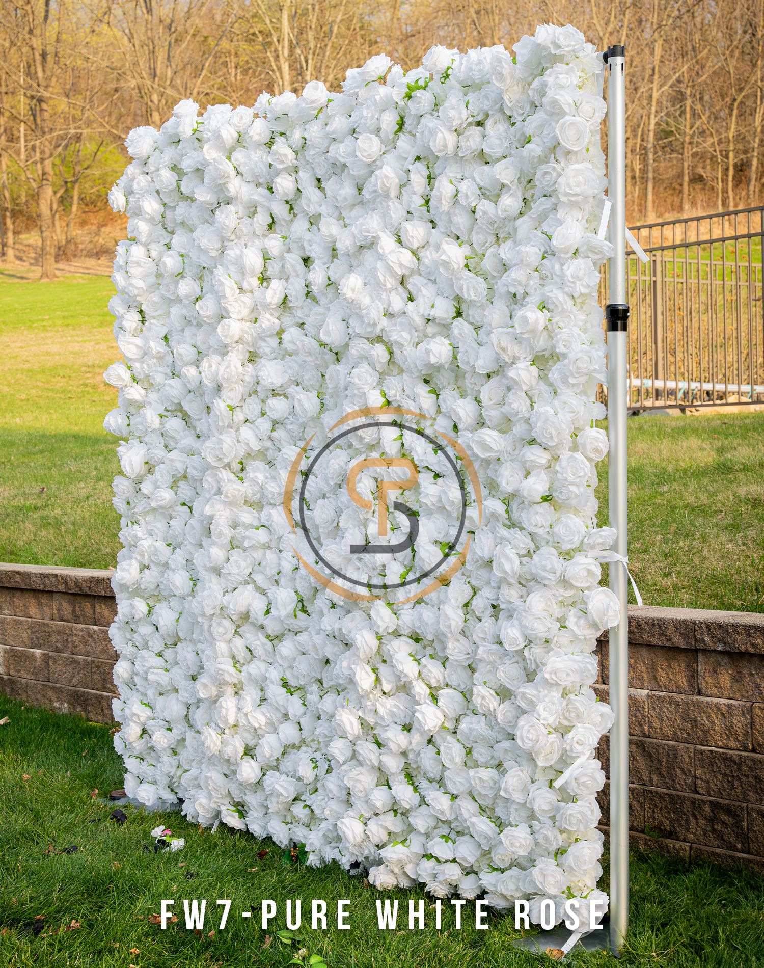 White flower wall backdrop with circular logo monogram against outdoor garden setting.