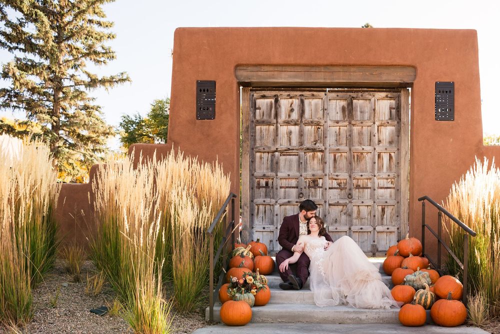 Couple sitting by rustic wooden door decorated with fall pumpkins at adobe style venue.