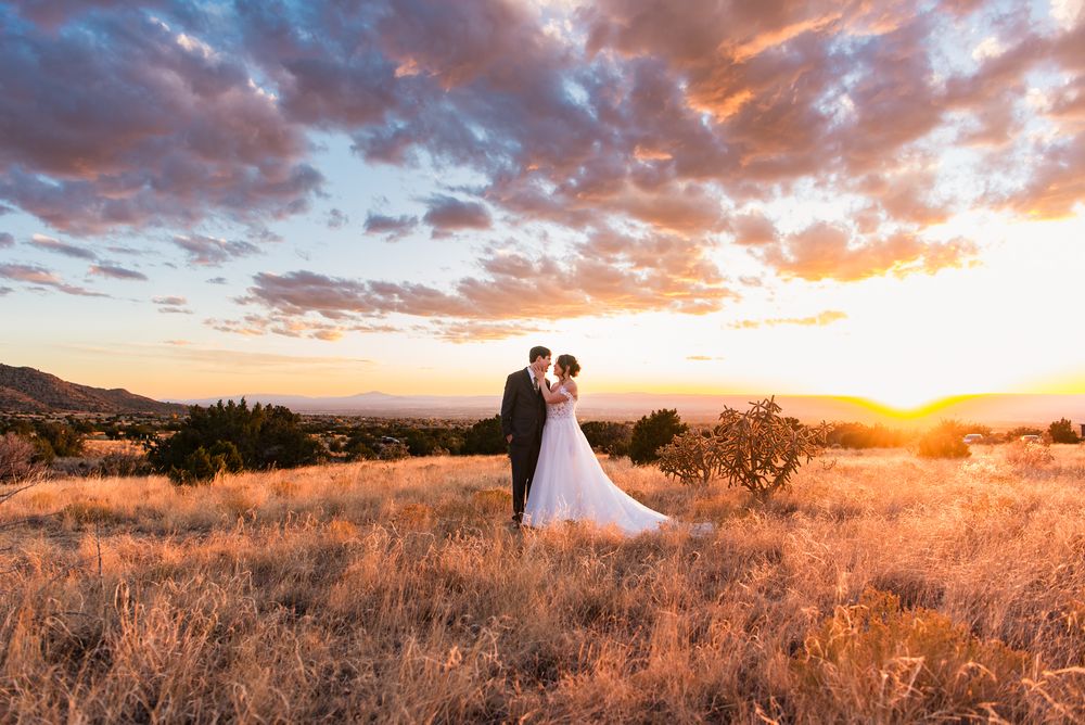 A couple in wedding attire silhouetted against a dramatic sunset sky over golden California grasslands at dusk.