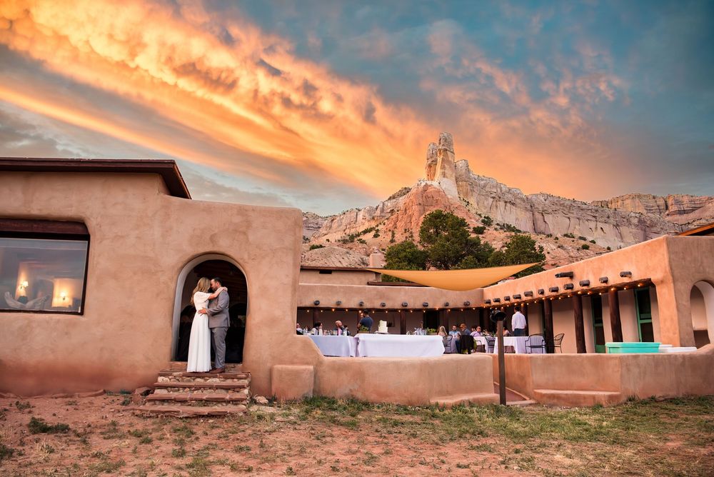 Wedding couple standing in adobe doorway with dramatic mountain sunset and string lights.