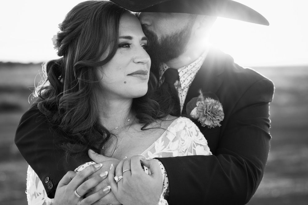 A romantic black and white wedding portrait captured during golden hour with a soft sun flare in the background.