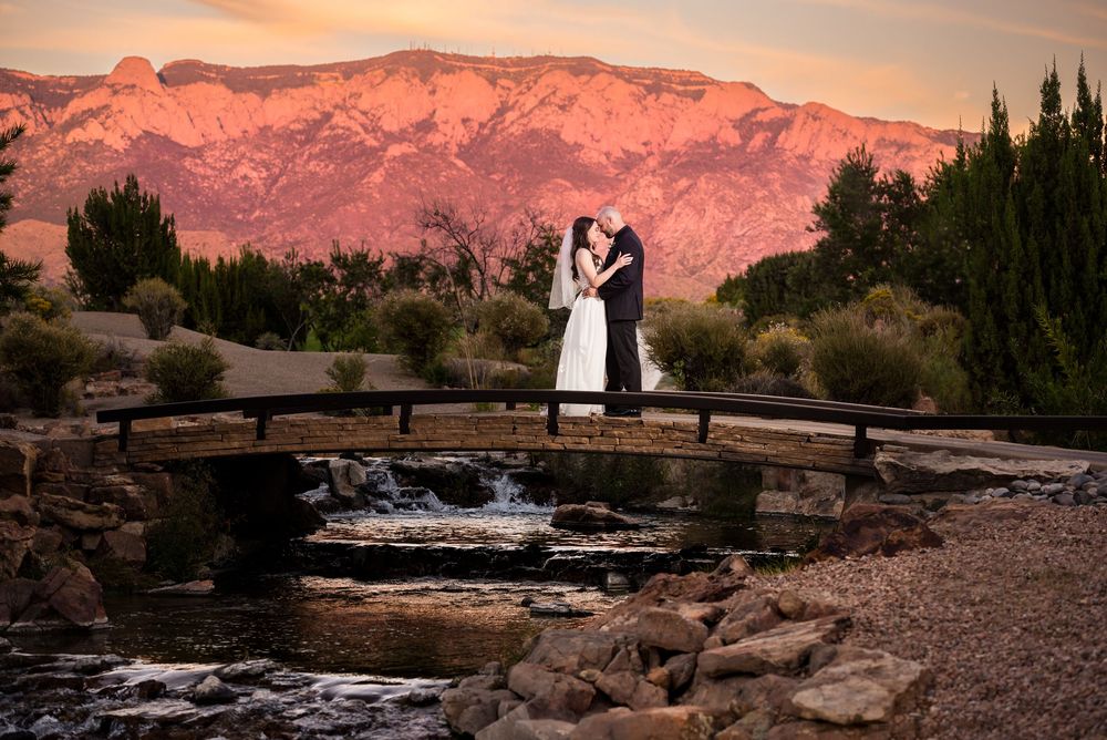 Silhouetted couple on stone bridge against mountain backdrop during sunset.
