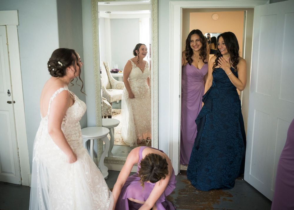 Wedding party members in purple and navy gowns share a candid moment in a bridal prep room.