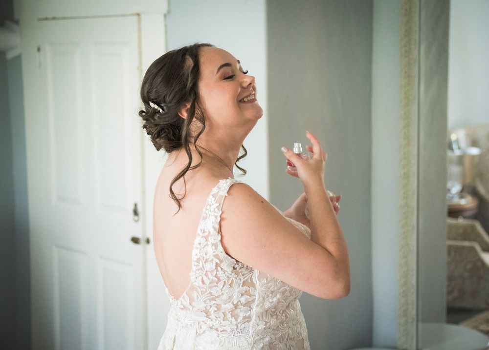 A bride in a delicate lace wedding dress laughs joyfully during a candid getting-ready moment.