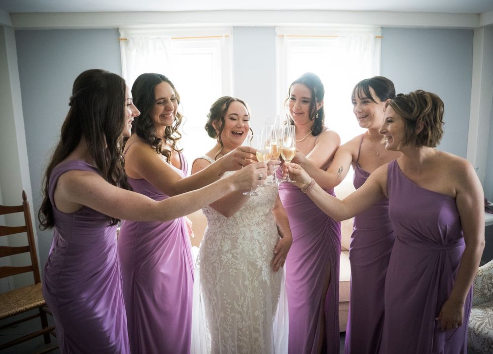 A group of bridesmaids in matching purple dresses raise champagne glasses in celebration at a wedding.