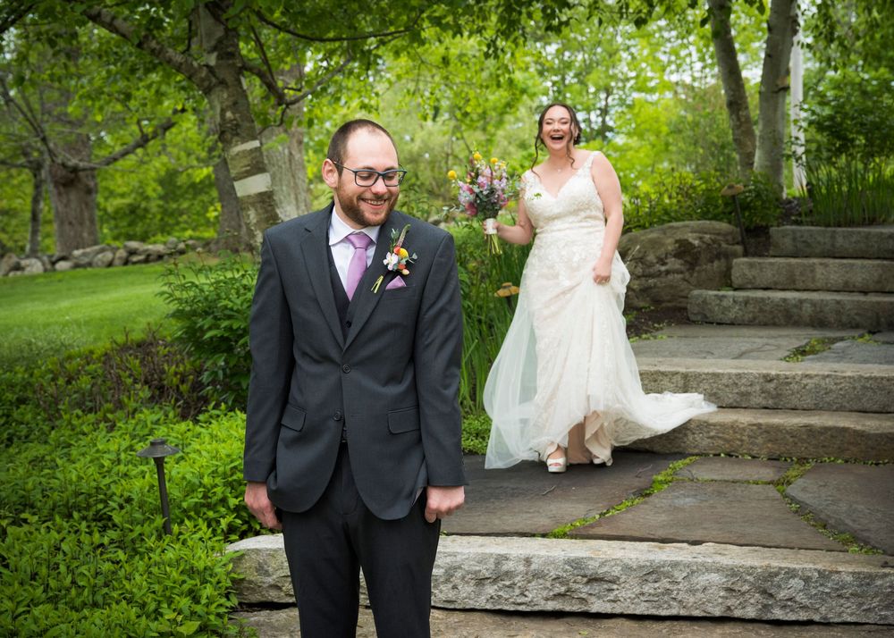 First look wedding photograph showing a couple on stone steps surrounded by lush green foliage in an outdoor garden setting.