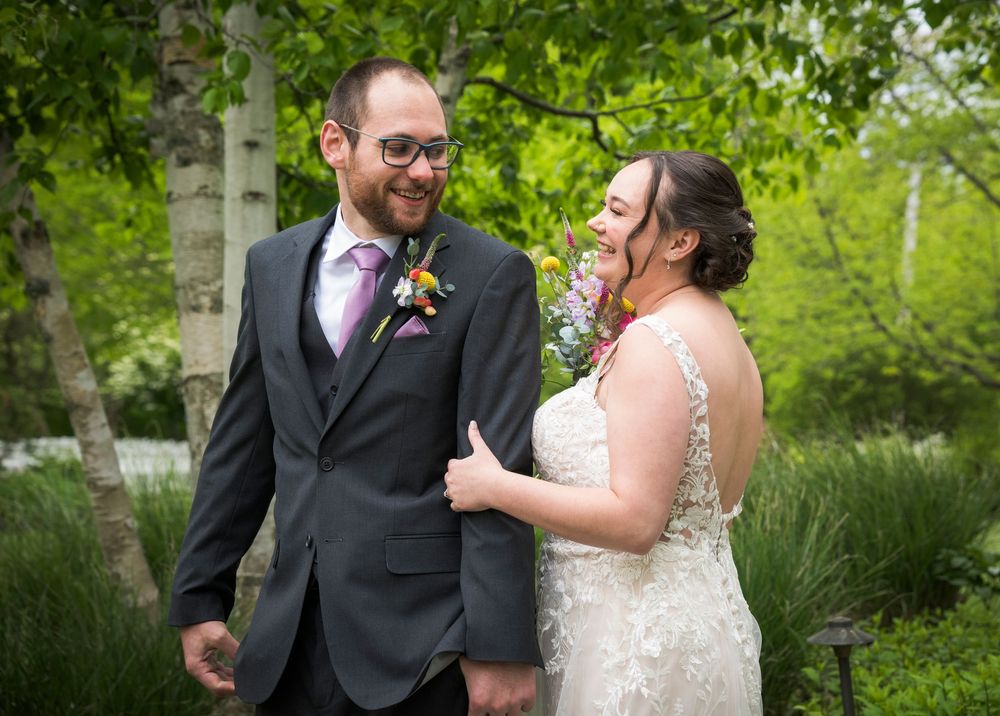 A bride and groom share a joyful moment together in a garden setting with lush green foliage in the background.