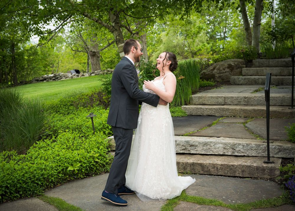 A celebratory couple shares a special moment on stone garden steps surrounded by lush greenery at an outdoor venue.