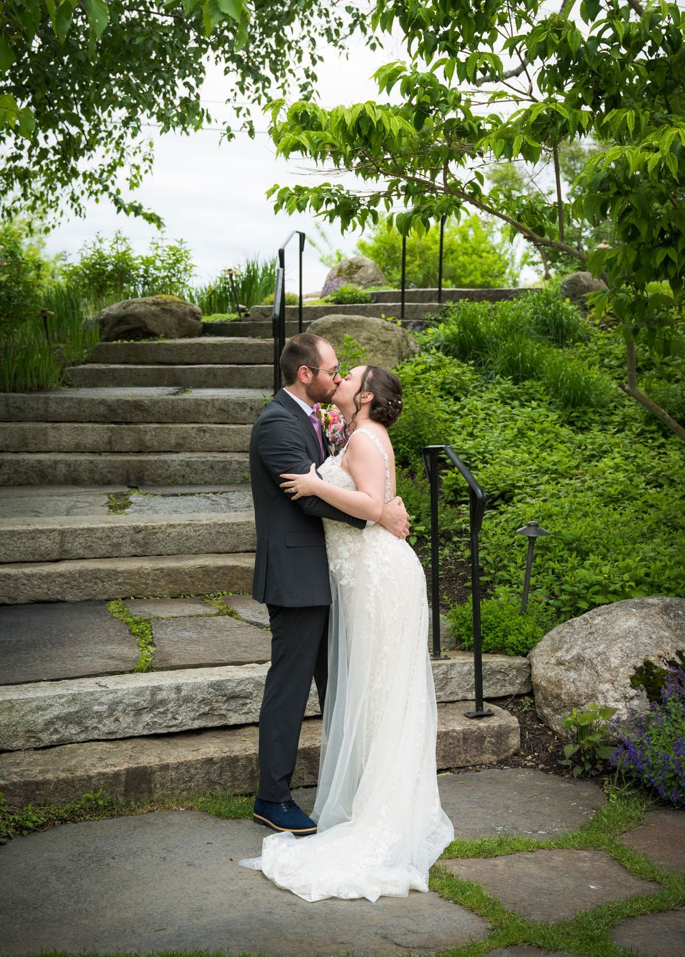 Romantic moment captured on stone garden steps surrounded by lush greenery and blooming spring flowers.