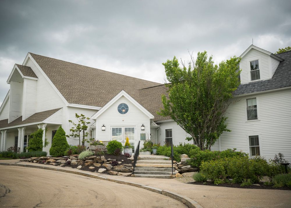 A white church building with steep rooflines and landscaped grounds featuring stone retaining walls and greenery.